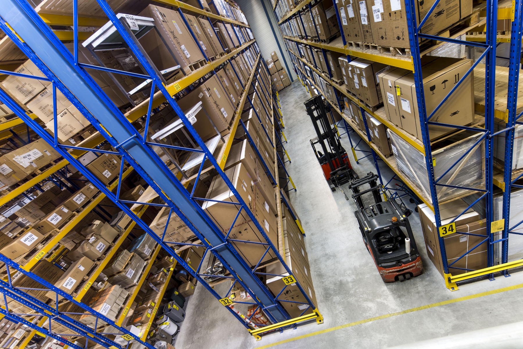 magazijn met hoge stellingen vol dozen en een heftruck in het gangpad van het distributiecentrum