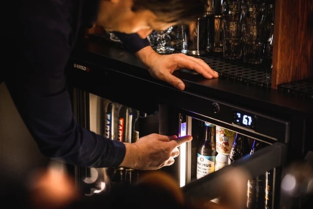 Bartender plaatst flessen in een Gamko barkoeling met digitale temperatuurweergave in een professionele baromgeving.