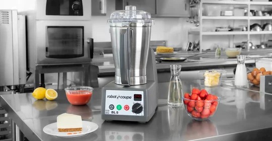 Robot Coupe blender op een roestvrijstalen werkbank met aardbeien, citroenen en andere ingrediƫnten in een professionele keuken.