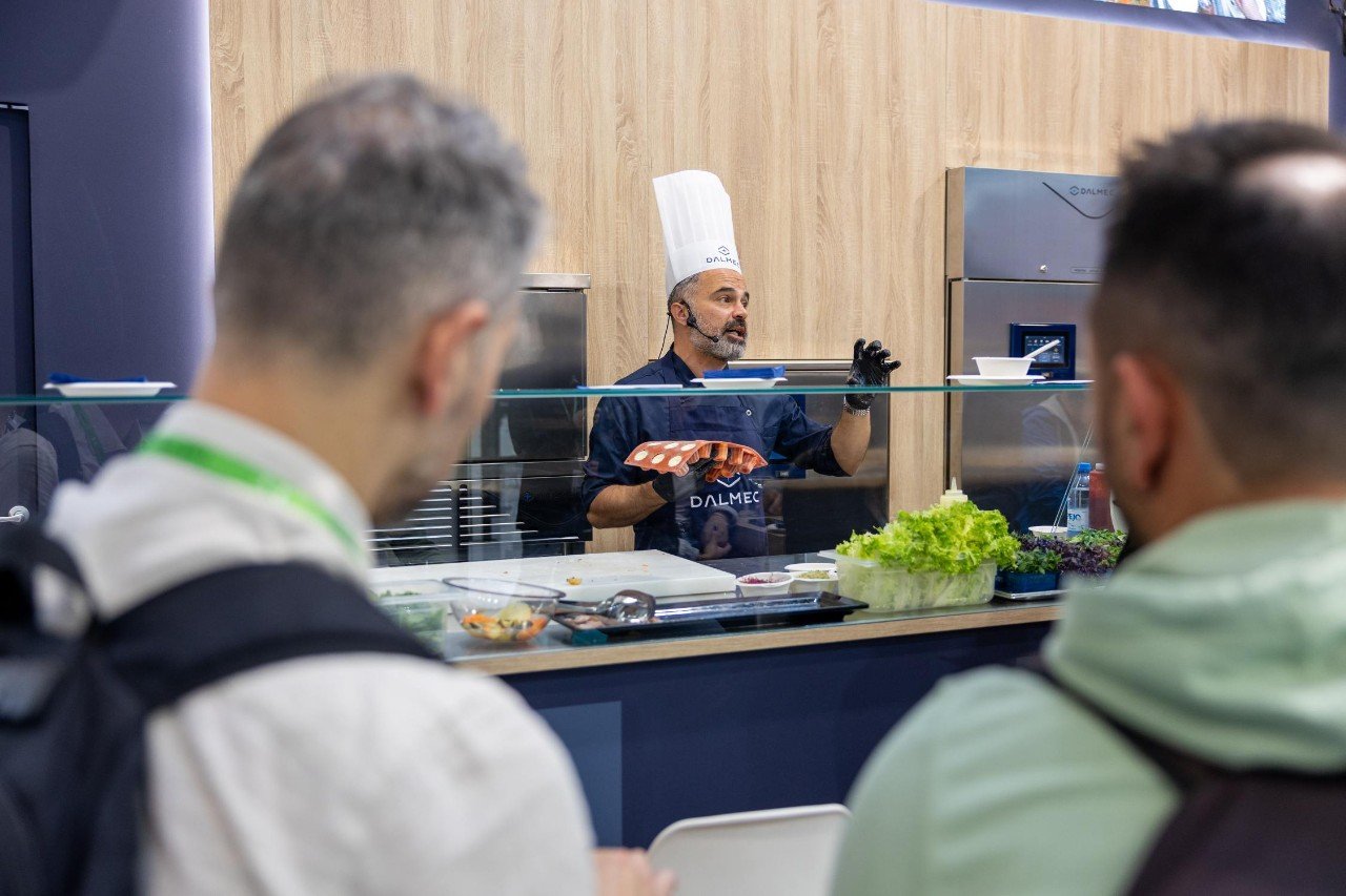 Chef geeft een kookdemonstratie op een HostMilano, terwijl bezoekers toekijken bij een professionele keukenopstelling.